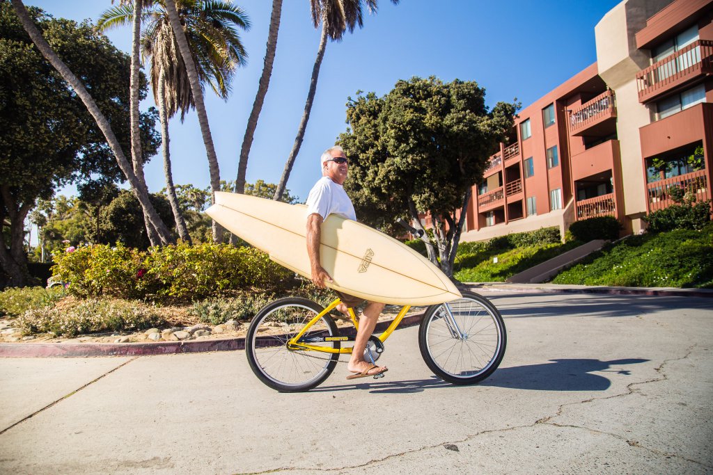 john holding surfboard on bike at c street